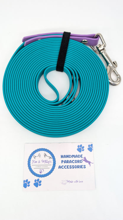 Blue paracord dog leash with purple handle and metal clip on a white background with brand card.